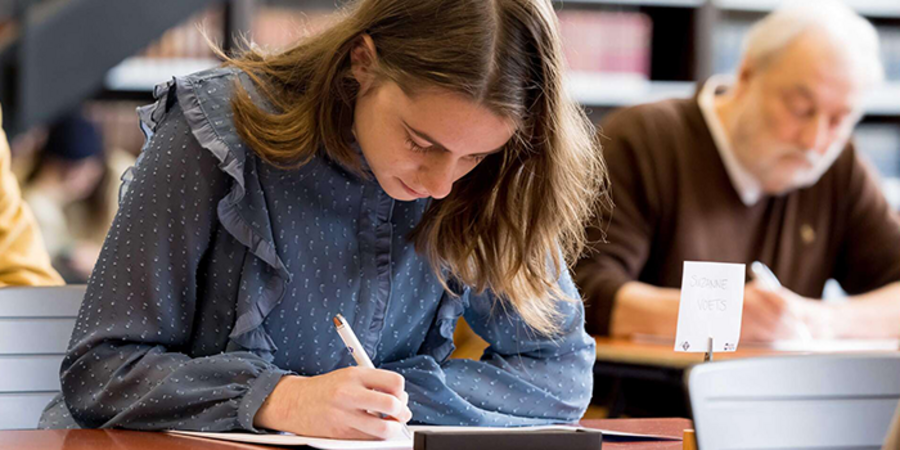 STOCK: Meisje met blauwe blouse schrijft voorovergebogen iets op papier voor haar